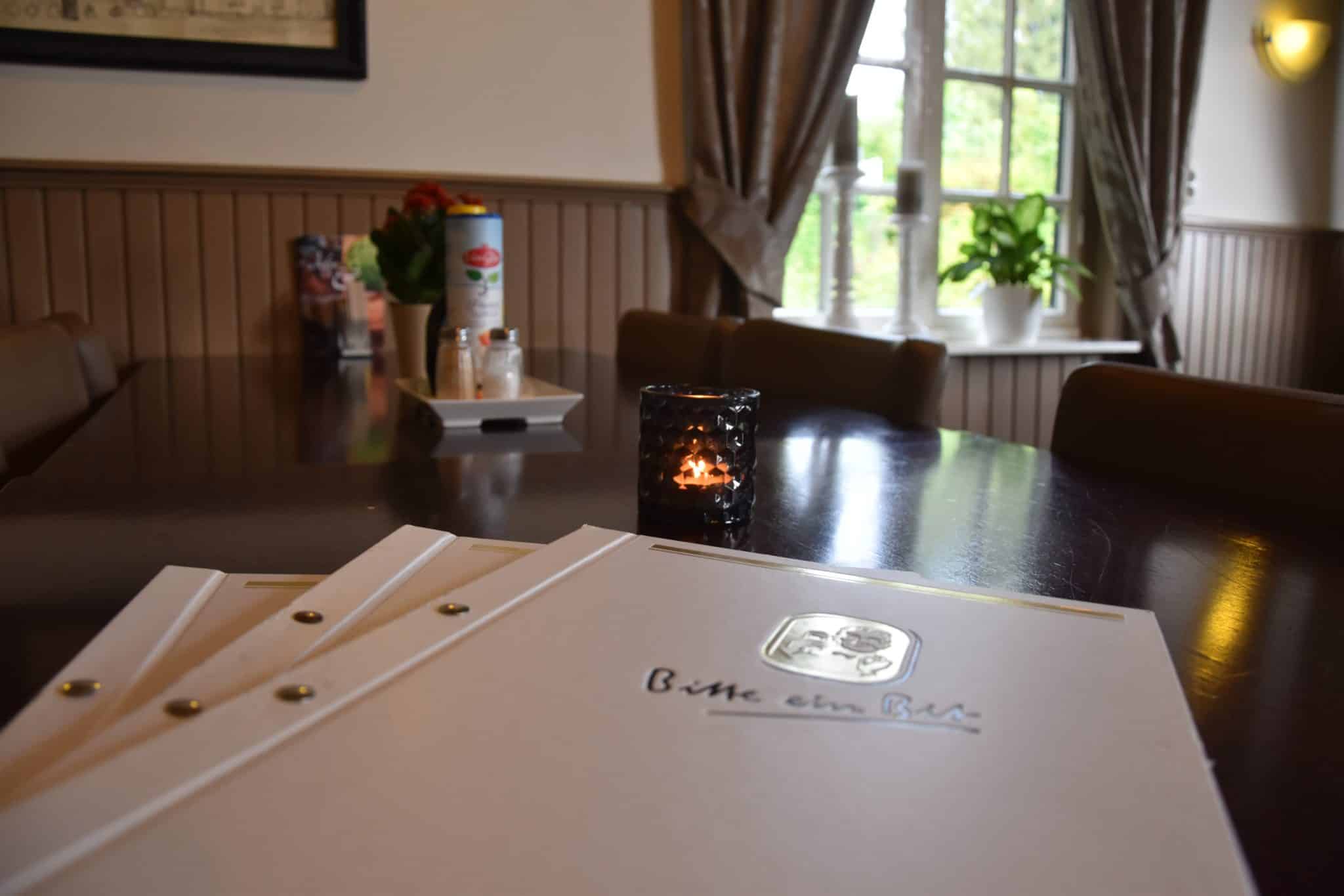 Menukaarten en een waxinelichtje op een gedekte tafel bij het raam in het restaurant.
