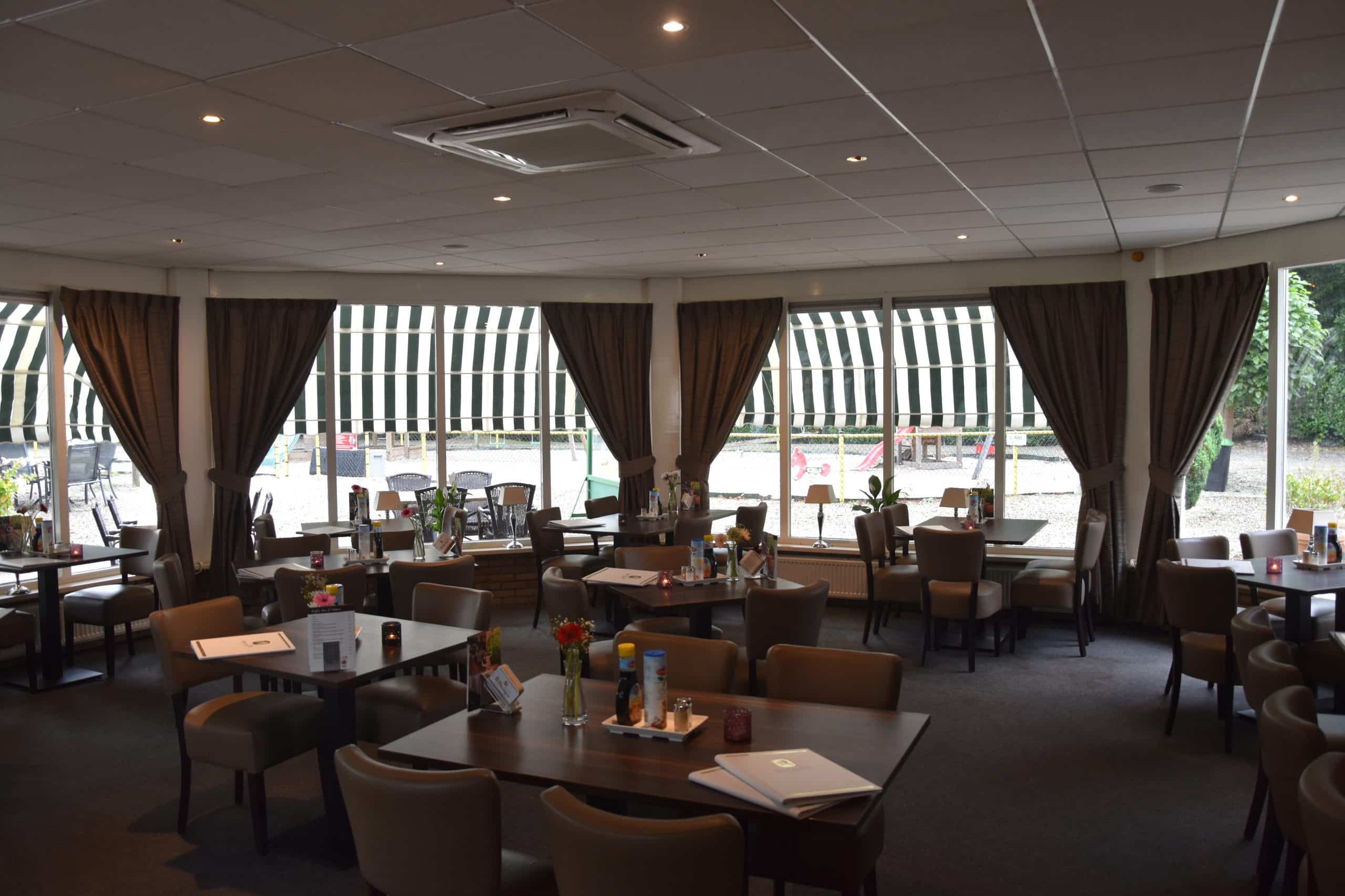 Het restaurant van binnen, met gedekte tafels en uitzicht door de ramen op het terras.
